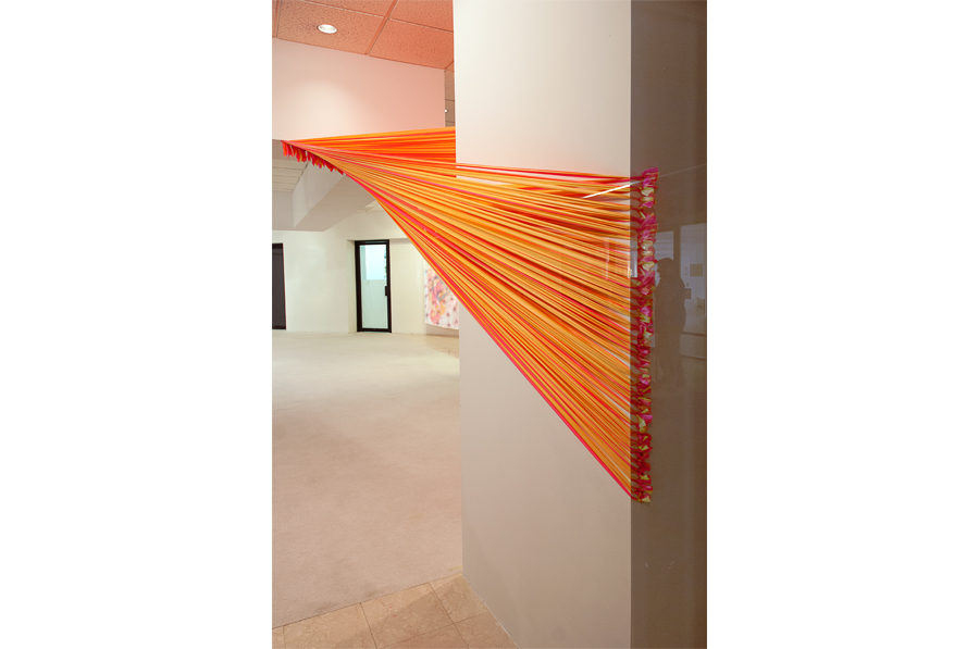 Florescent pink and yellow strands of flagging tape stretch from a plane in the ceiling to a column where it wraps around the rear corners and terminates in a series of eye hooks.