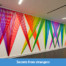 A rainbow hued wall weaving of plastic flagging tape on view at the Wells Fargo Center in Los Angeles, CA